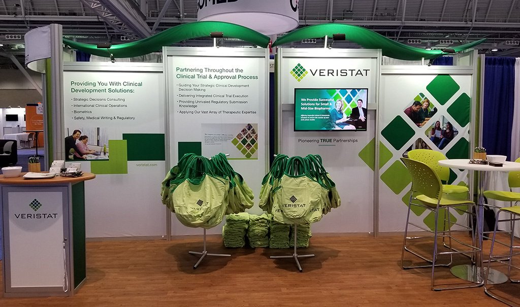 Veristat custom modular aluminum extrusion booth with graphics, monitor, counters, seating area, and wood-look  comfort flooring